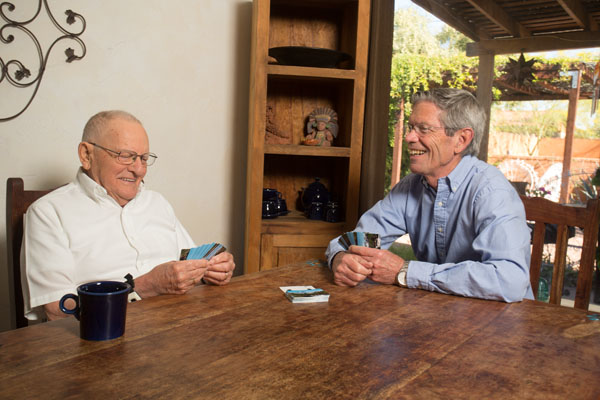 An older man laughs with a middle-aged man as they play cards