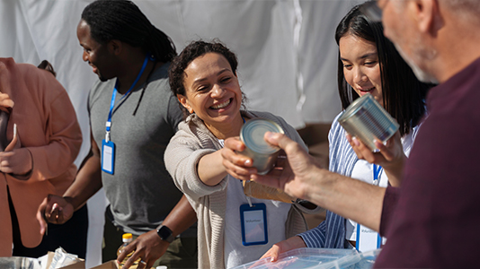 A group of people with name badges participating in a community service or food distribution event and handing out canned goods.