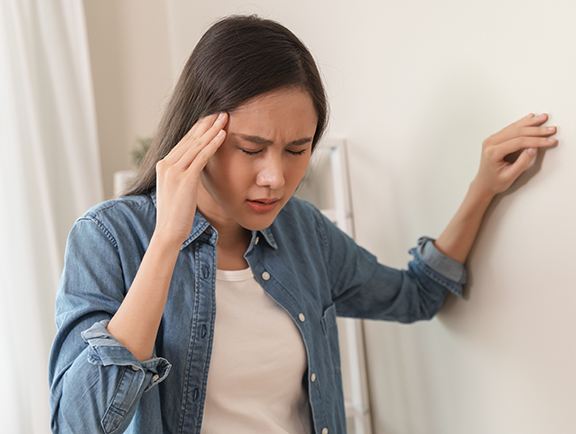 Woman bracing herself on wall and holding head