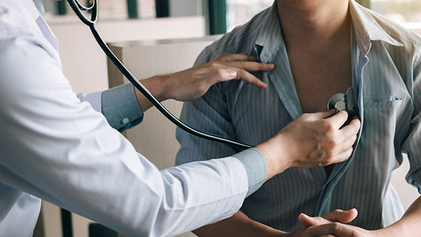 Person using a stethoscope to listen to another person's heart in a medical setting.