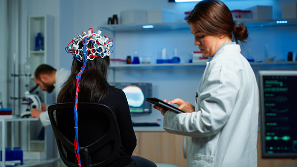 Researchers in a lab conducting an experiment with a woman wearing a cap connected to wires.