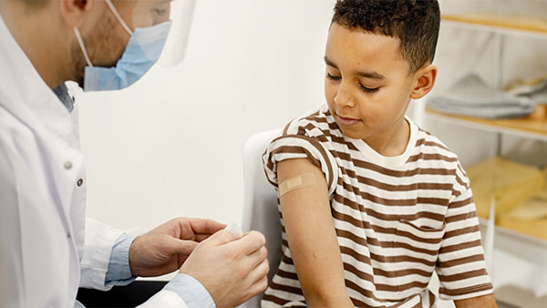  A young boy with a bandage on his arm and a medical professional beside him.