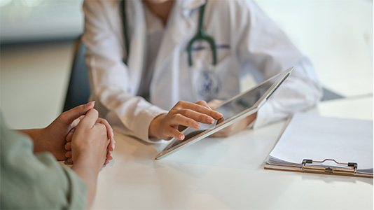 Healthcare professional using a tablet during a consultation with a patient.