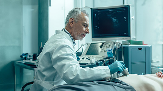 A technician performing an abdominal ultrasound on a man's abdomen in a well lit room.