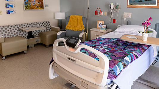 A well lit and brightly decorated hospice room. A colorful new quilt is placed on the bed.