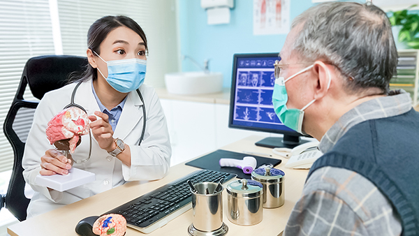 Doctor explaining a brain model to a patient at a desk in a clinic.