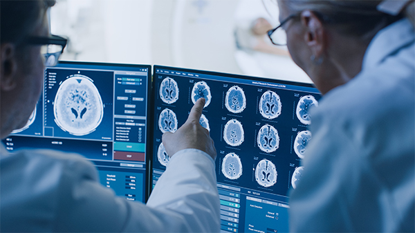 Two medical professionals reviewing brain scans on computer monitors.