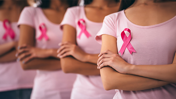 Four women in light pink t-shirts with pink ribbons pinned to their chests, arms crossed.