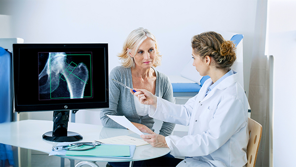  A doctor explains medical information to a patient, with a hip X-ray displayed on a computer monitor.