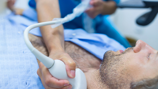 A hand holds an ultrasound wand to a man's neck