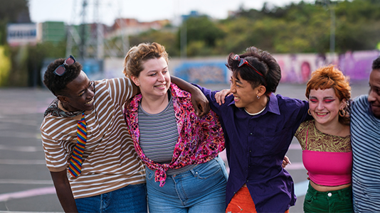 A diverse group of teenagers laughing with arms around each other on an outdoor court.