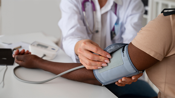 A nurse adjusts medical equipment next to a seated patient with a blood pressure cuff on his arm.