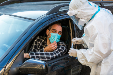 A masked individual in a car talking to a medical profession in PPE