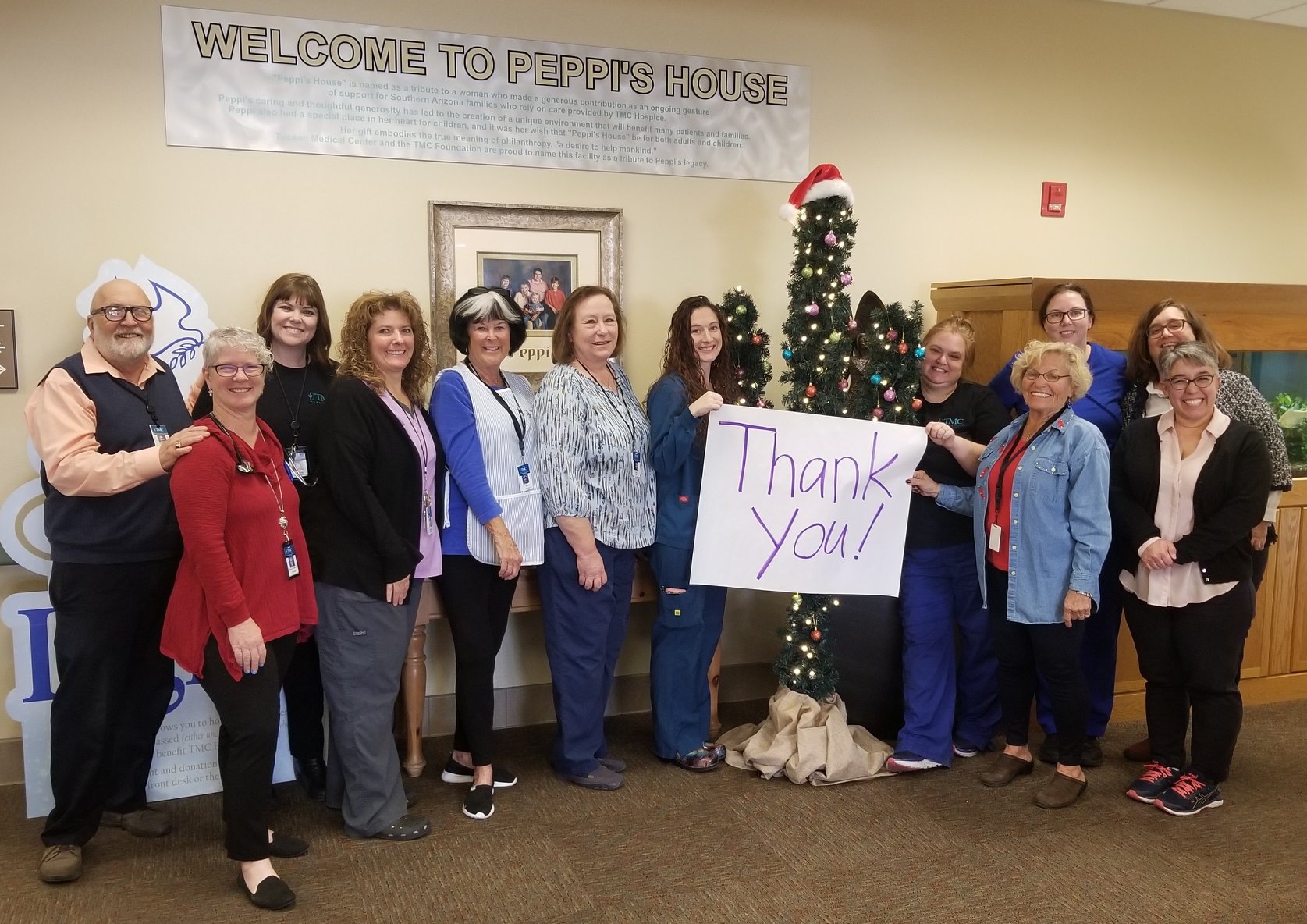 Staff at Peppi's House Hospice gather around a cactus shaped Christmas tree holding a "Thank you" sign for volunteers.