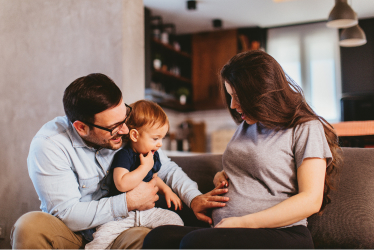 A father and child touching the pregnant belly of a mother