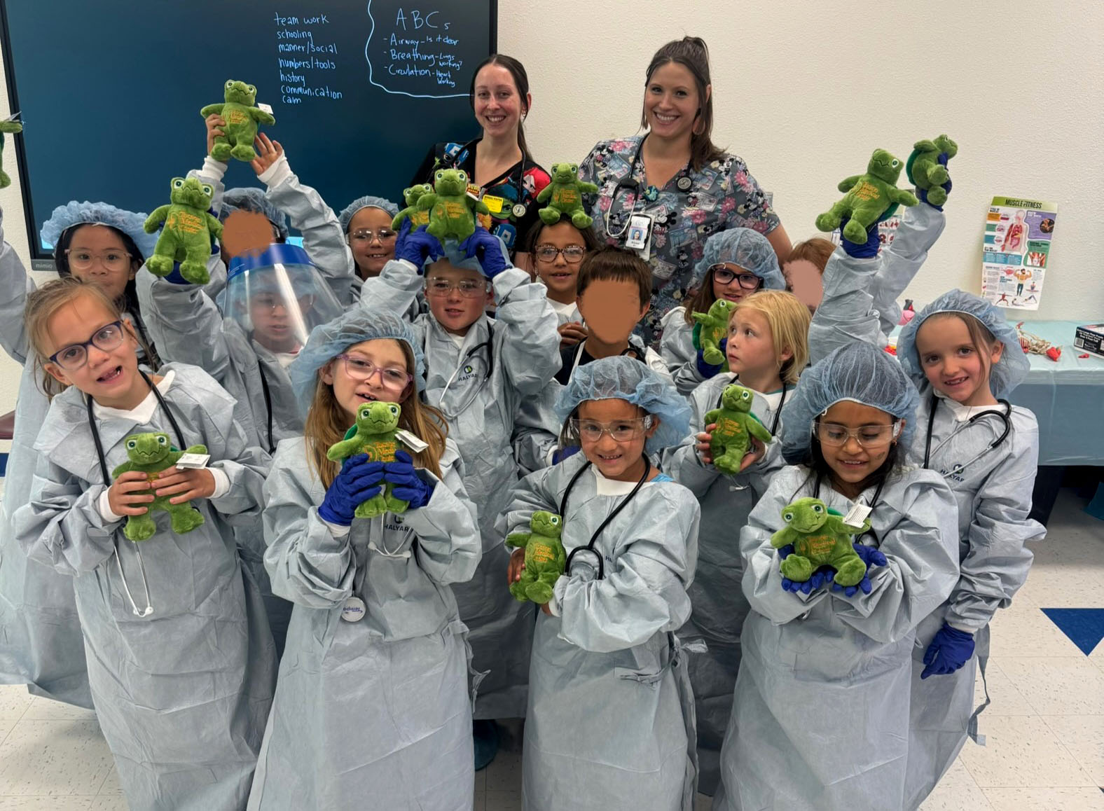 Second grade students dressed up in surgical gowns hold up plush turtles
